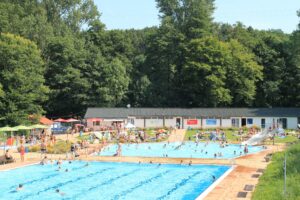 Das Waldfreibad, im Vordergrund das große Schwimmbecken, im Hintergrund das Nichtschwimmerbecken und die Umkleiden.