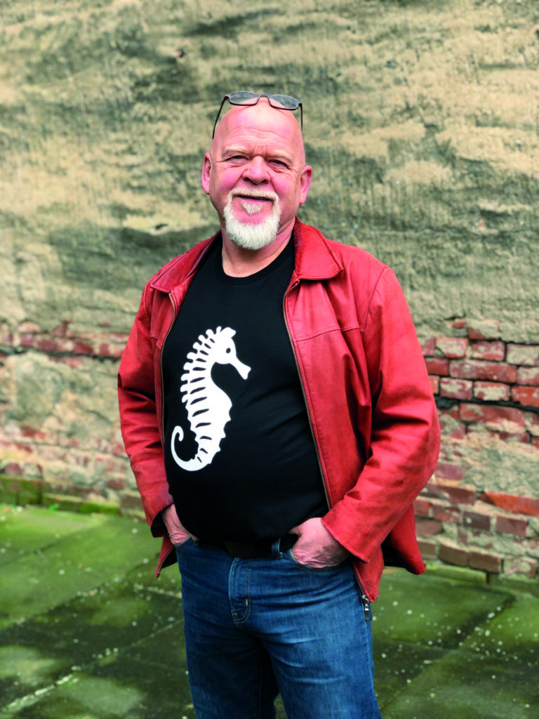 Ein Mann mit Brille auf dem Kopf und einem Seepferdchen auf dem T-Shirt. Rote Jacke.